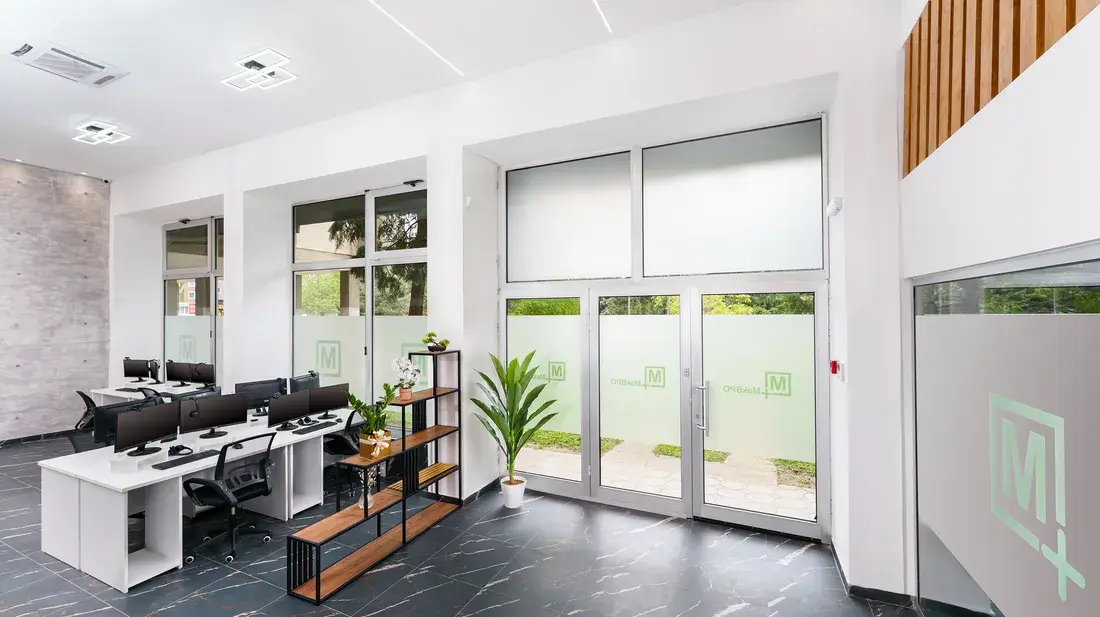 A work area at the MakBPO office in Bitola, with desks, plants, and daylight from full height windows.